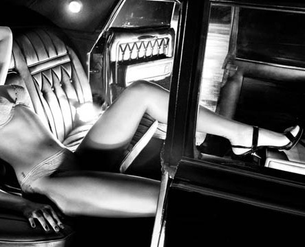 A lower torso of a sexy slim female wearing panties in a limo with the door open. Her head is not visible she is wearing a high heeled shoe with a strap and silk underwear the picture is black and white
