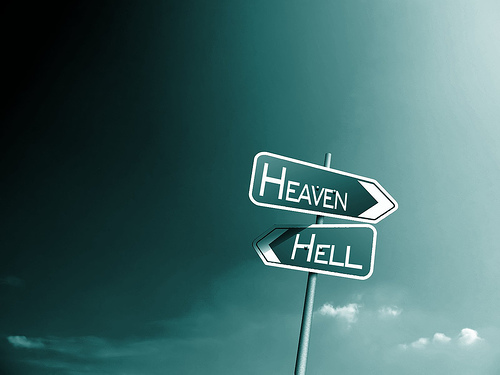 A road sign set against a cloud backdrop one sign points right and says heaven one sign points left and say hell.