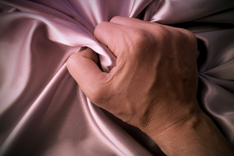 Man grabing satin sheet on the bed.